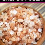 Close up of pink Himalayan salt in a small wood bowl on a wood table that are scented with essential oils