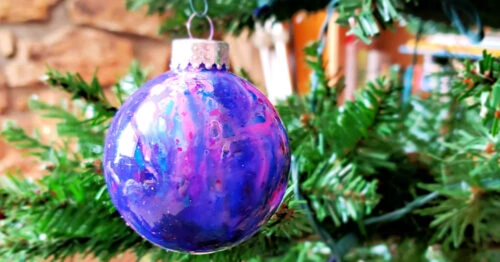 Melted crayon galaxy ornament hanging on a Christmas tree in front of the fireplace.