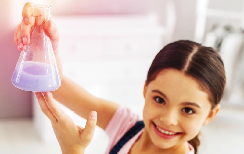 Girl holding up a beaker with lavender fluid in it.