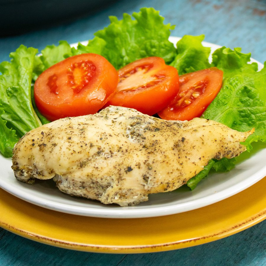 Seasoned chicken breast on a white plate with tomatoes and lettuce that was cooked in an Instant Pot pressure cooker
