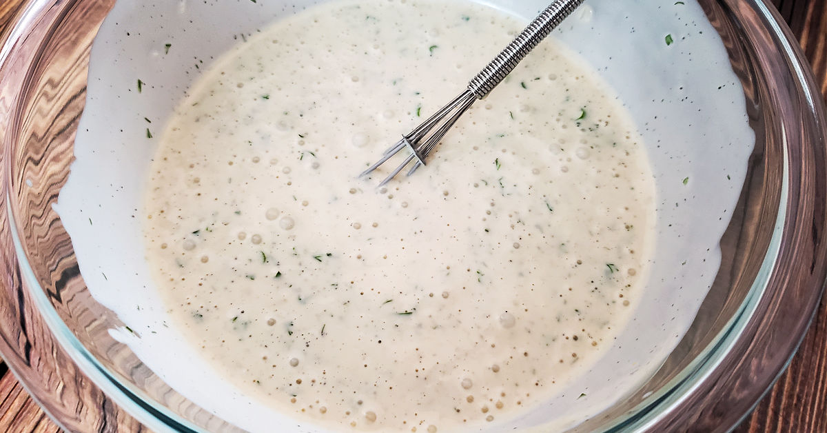 Homemade ranch dressing being whisked in a glass mixing bowl.