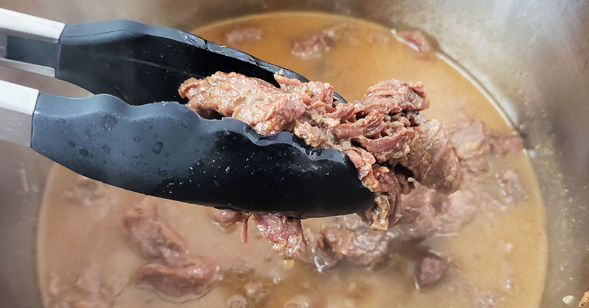 Cooked carne asada being removed from Instant Pot with tongs.