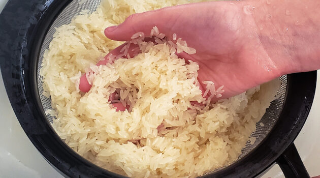 Hand in a strainer full of dry jasmine rice being rinsed.