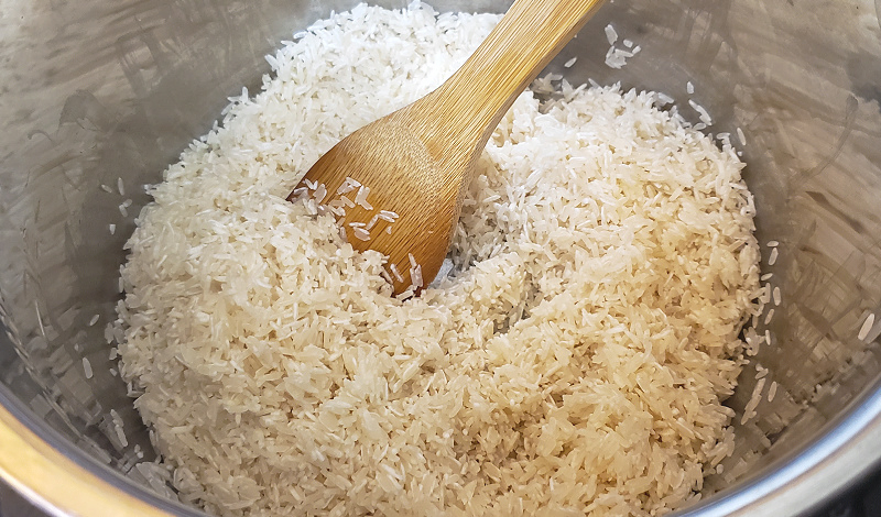 Jasmine rice being sauteed in an Instant Pot with a wooden spoon before being pressure cooked.