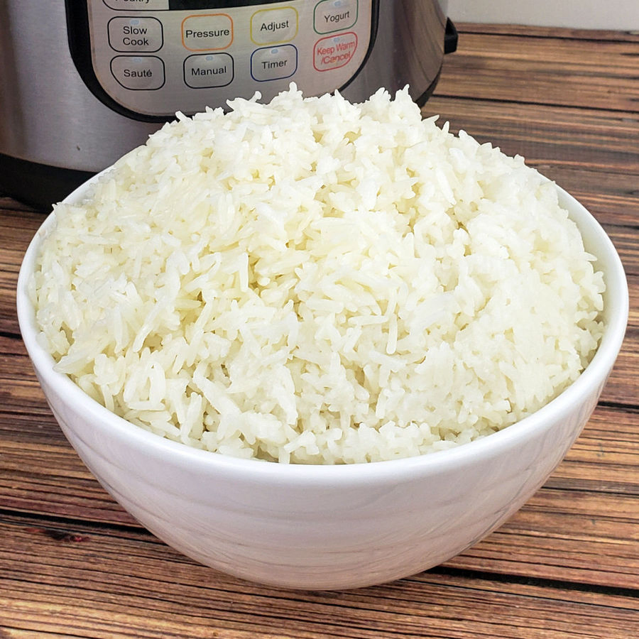 White ceramic bowl filled with jasmine rice in front of an Instant Pot on a brown wood table.