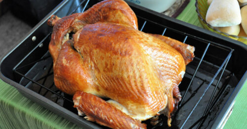 Thanksgiving turkey in roasting pan on table with green tablecloth.