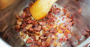 Bacon being sauteed in an Instant Pot with a bamboo spatula.