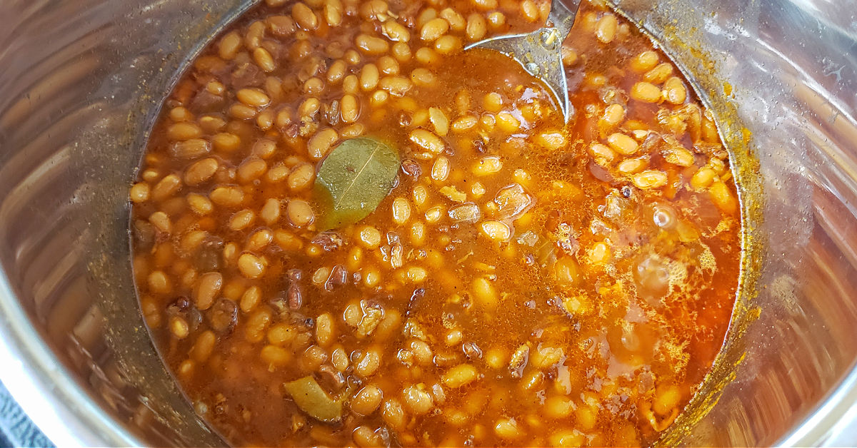 Cooked baked beans in Instant Pot with bay leaf floating in it.