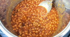 Baked beans being stirred in Instant Pot with stainless steel mixing spoon.
