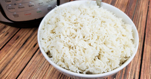Fluffy basmati rice in white serving bowl next to Instant Pot it was cooked in.