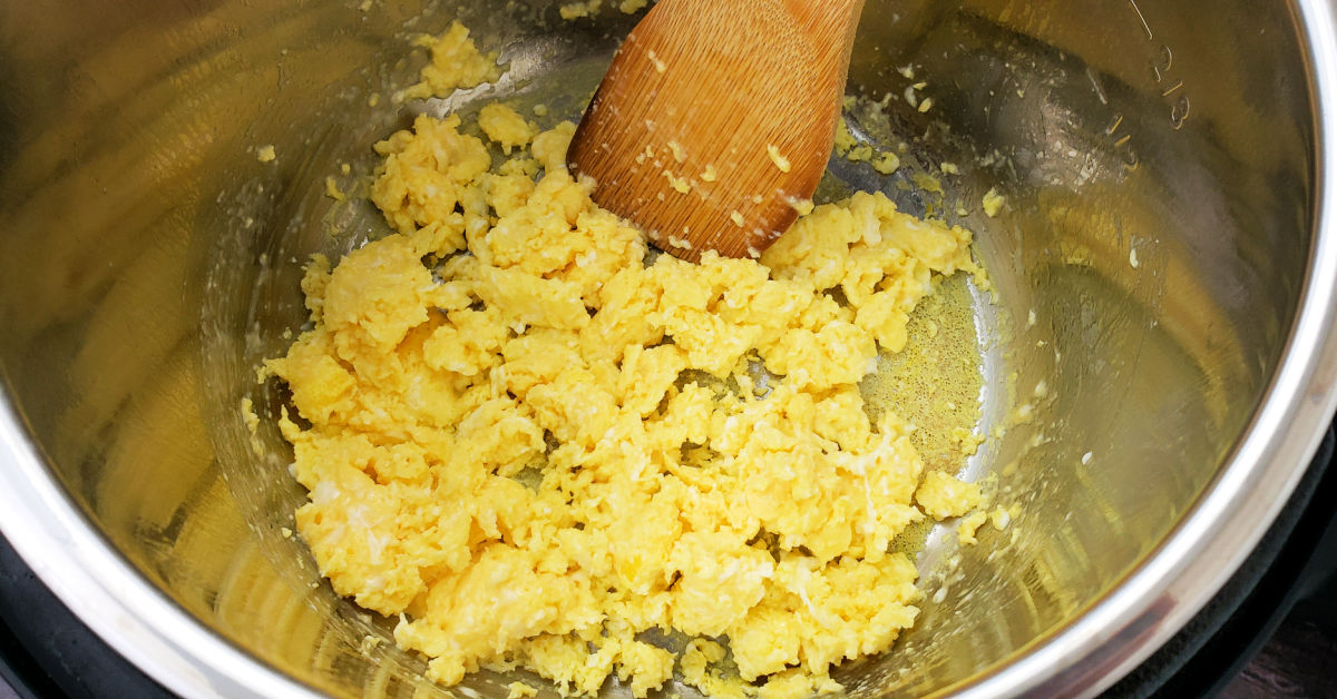 Scrambled eggs being fried in bottom of Instant Pot inner pan with bamboo spatula.