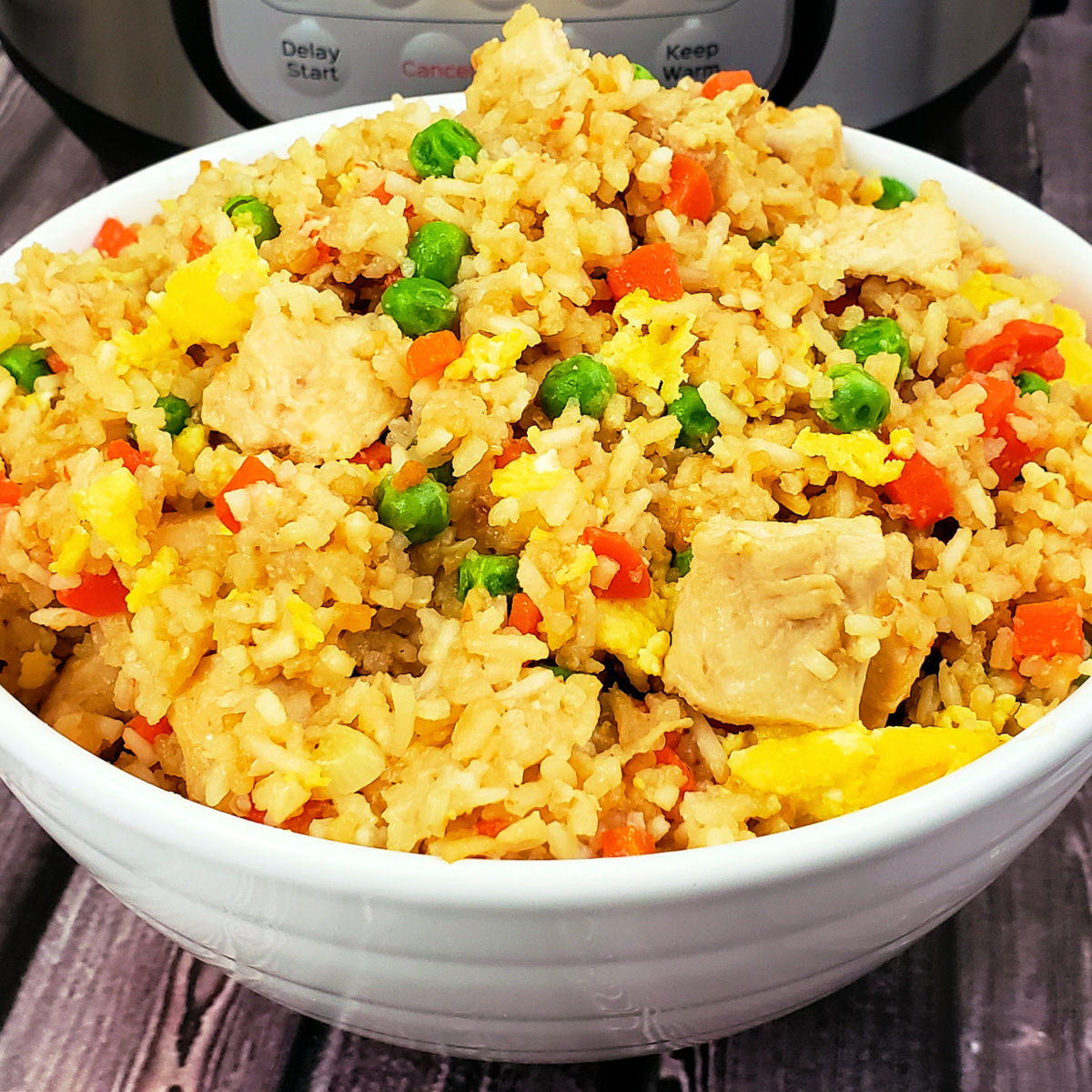 Chicken fried rice in white serving bowl in front of Instant Pot on table.