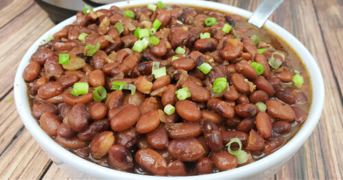 Pinto beans garnished with green onions in white serving bowl.