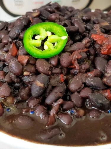 Black beans garnished with a jalapeno slice in a bowl with Instant Pot in background.