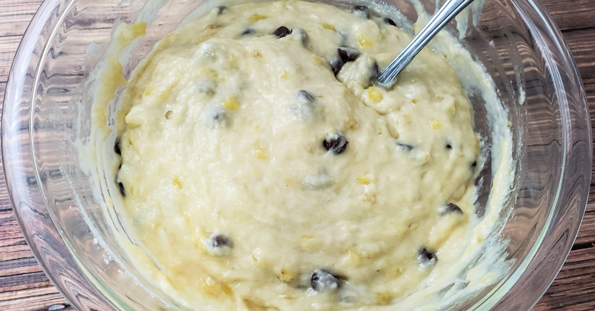 Chocolate chips being gently folded into banana muffins batter in mixing bowl.