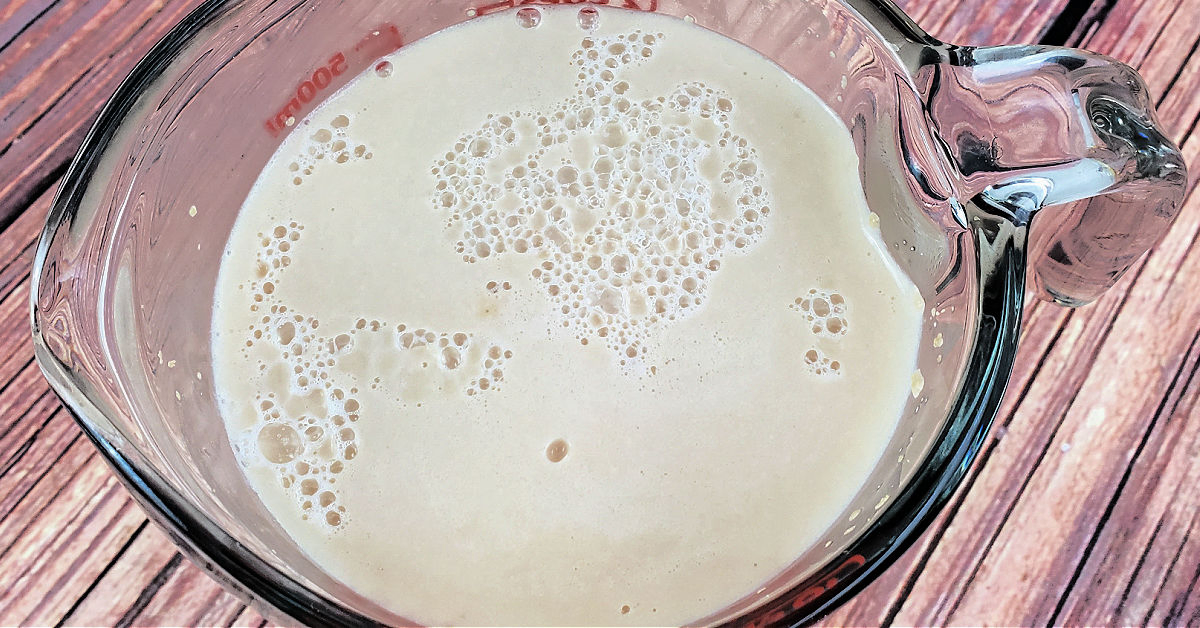 Yeast being proofed with warm water and sugar in glass measuring cup.
