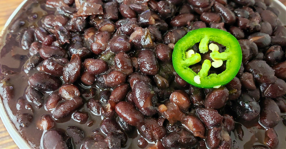 Close up of black beans cooked in an Instant Pot, topped with a jalapeno slice.