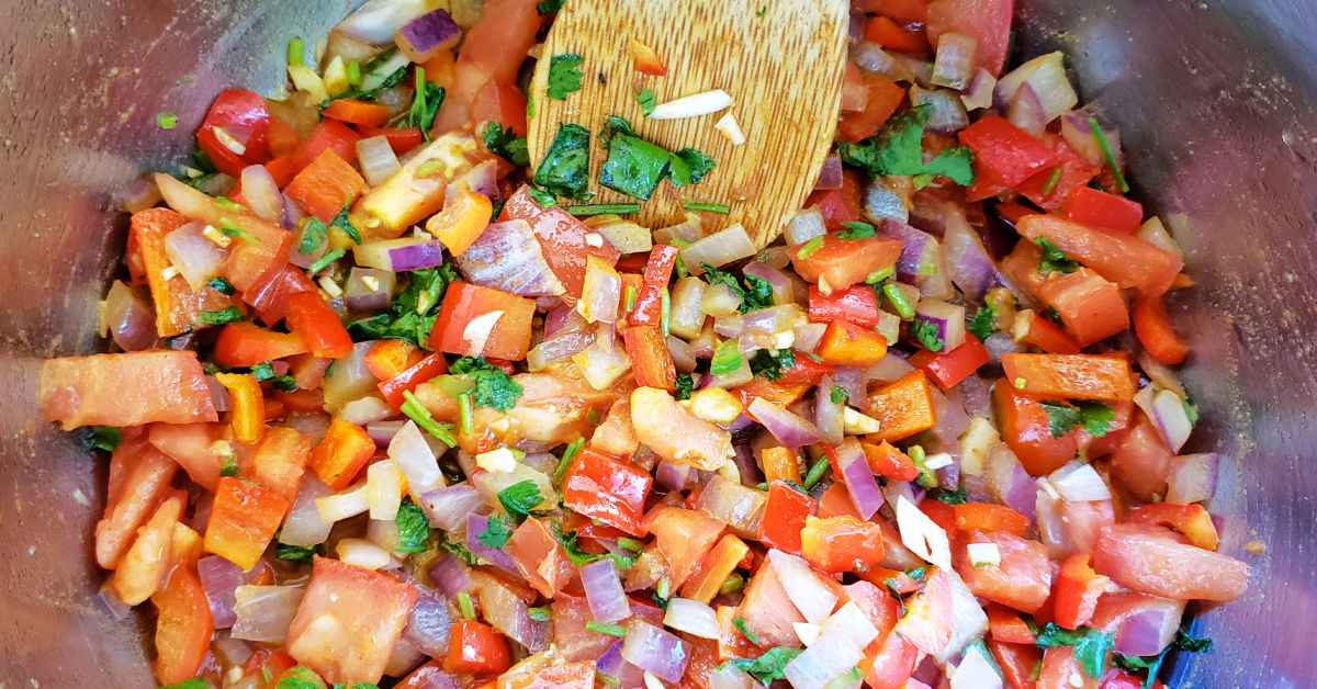 Tomato, garlic, jalapeno and cilantro being stirred into the onion and bell pepper mixture in the Instant Pot inner pan.