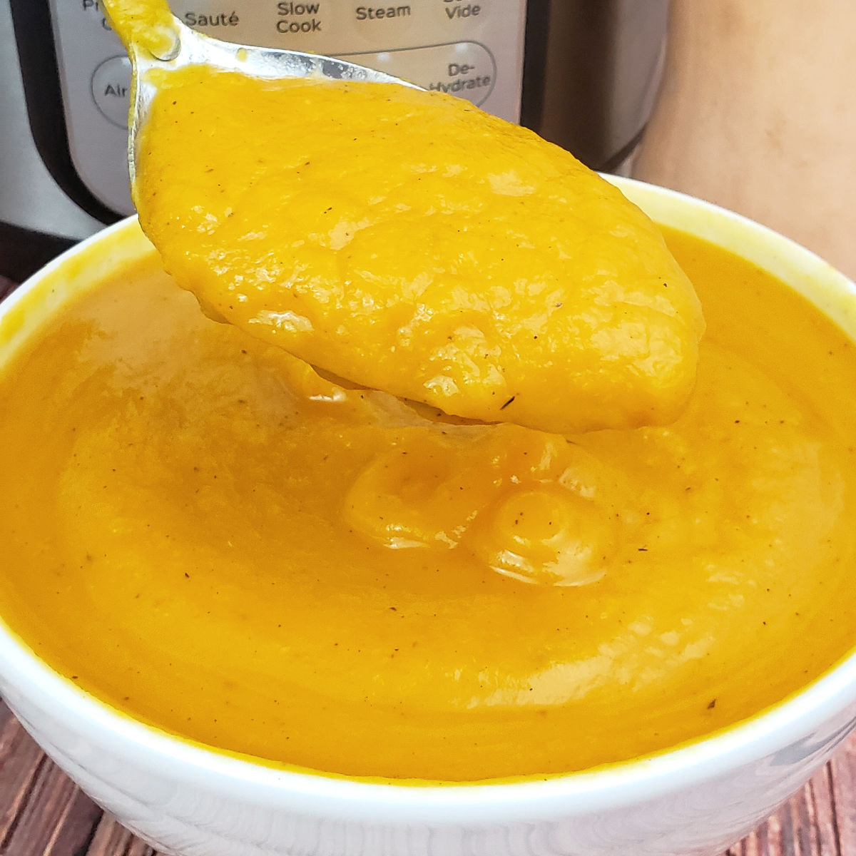 Butternut squash soup being served with a spoon in front of an Instant Pot.