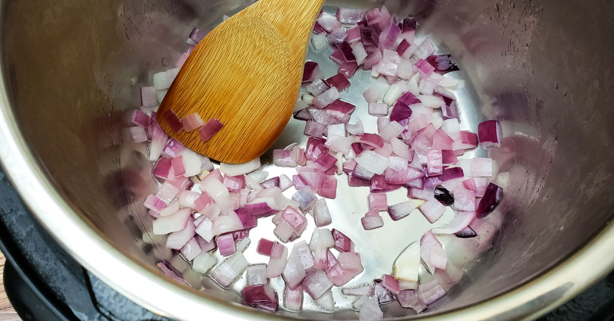 Purple onion being sauteed in Instant Pot inner pot with bamboo spatula.