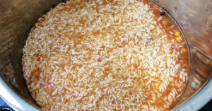 Uncooked jasmine rice pressed down under liquid for chicken burrito bowls in Instant Pot inner pan.