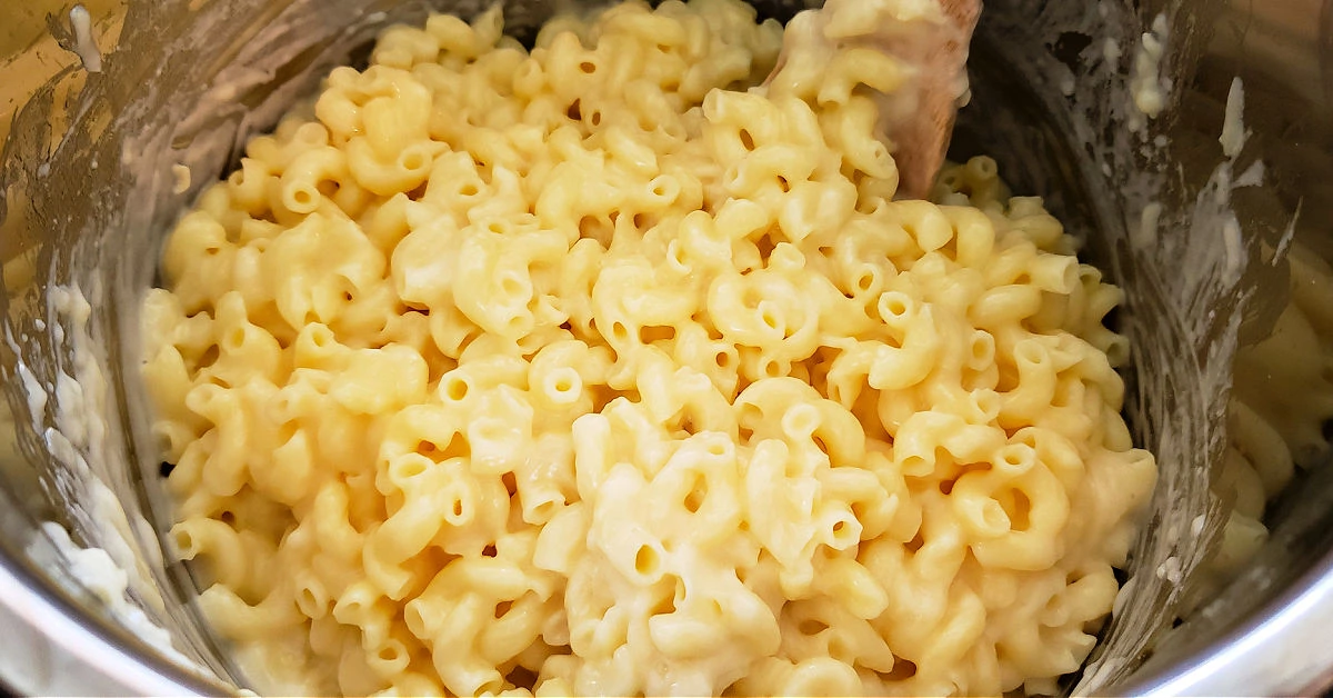 Grated cheese being stirred into elbow noodles in Instant Pot inner pan to make mac and cheese.