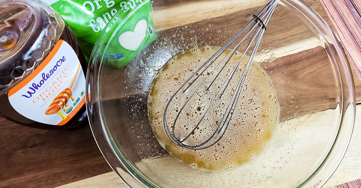 Eggs, sugar and honey being whisked in a mixing bowl.