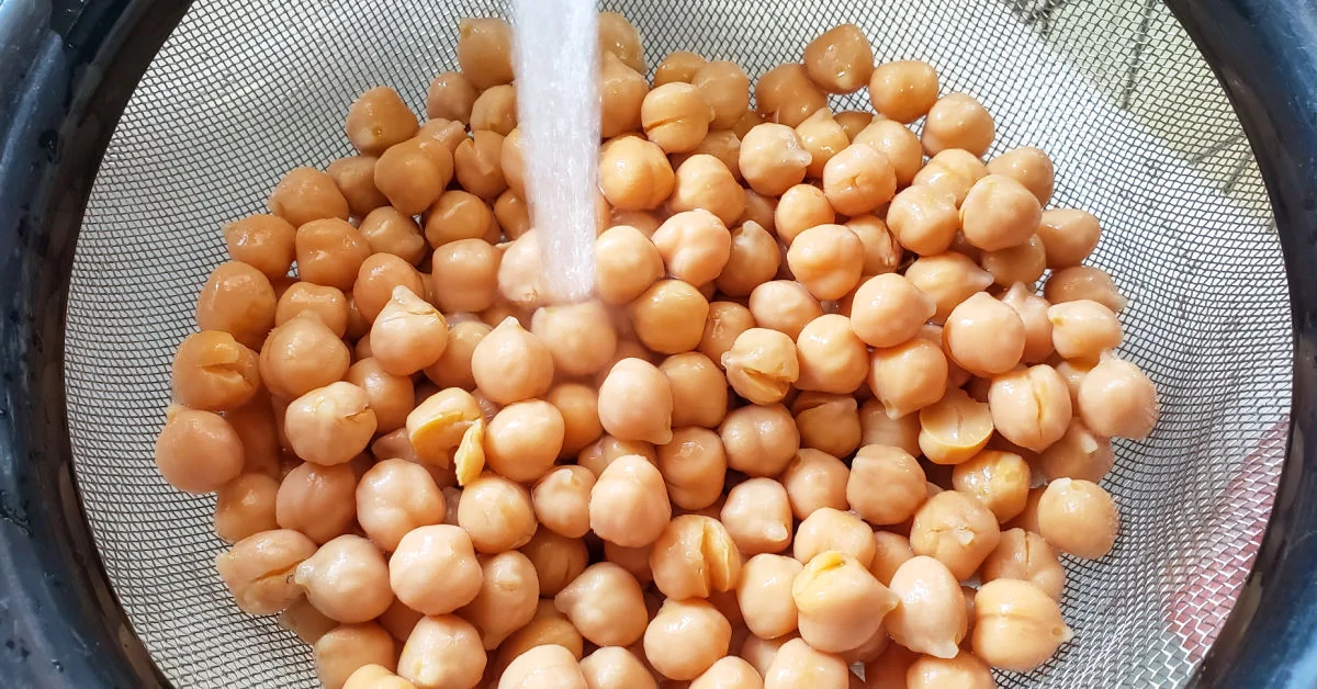 Canned chickpeas in strainer being rinsed with water.