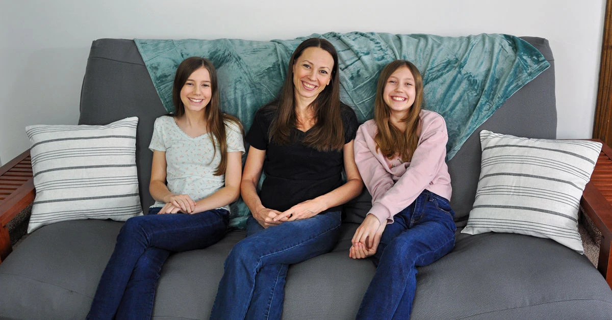 Chrystal, Zoe and Kaylee sitting with legs crossed on gray futon.