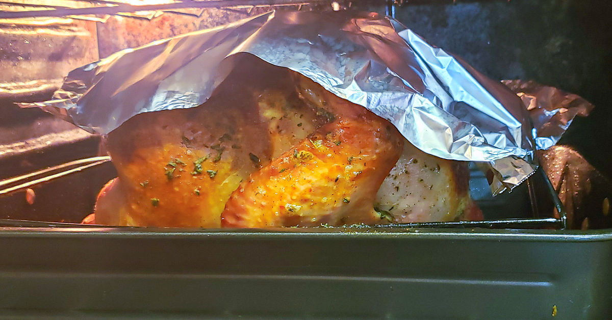 Turkey breast being shielded with aluminum foil from oven heat.