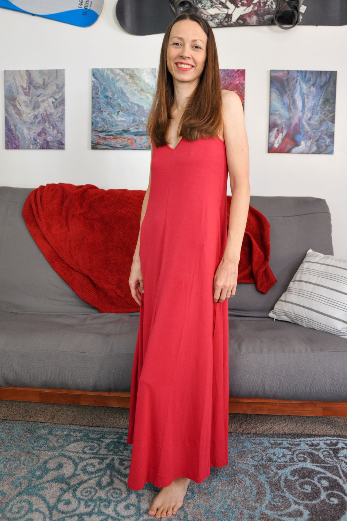 Chrystal standing in front of futon wearing Skivy's Goddess Gown in Crimson.
