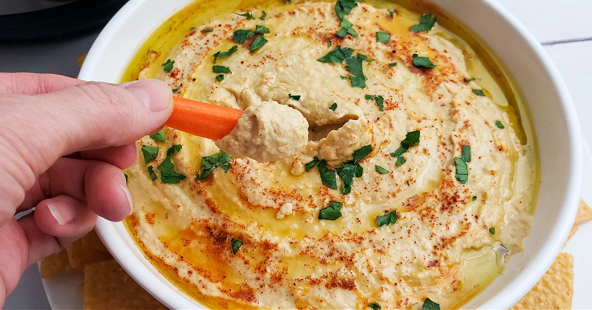 Hummus being dipped into with a carrot stick.