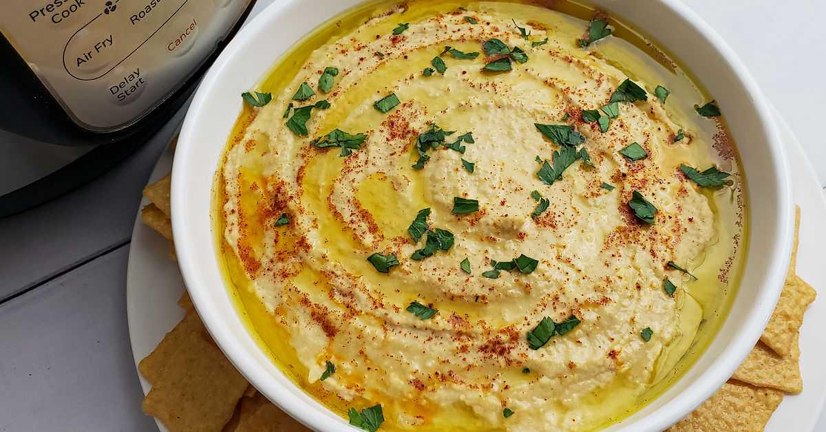 Hummus made in Instant Pot and served in white bowl garnished with olive oil, paprika and parsley.