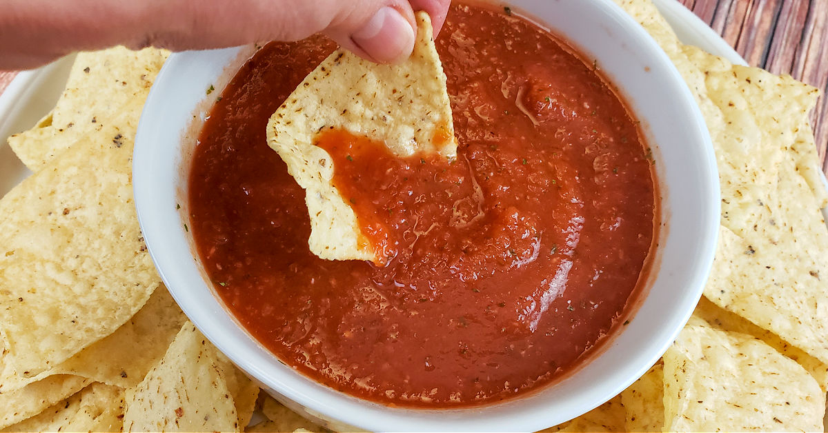 Tortilla chip being dipped in Mexican salsa.