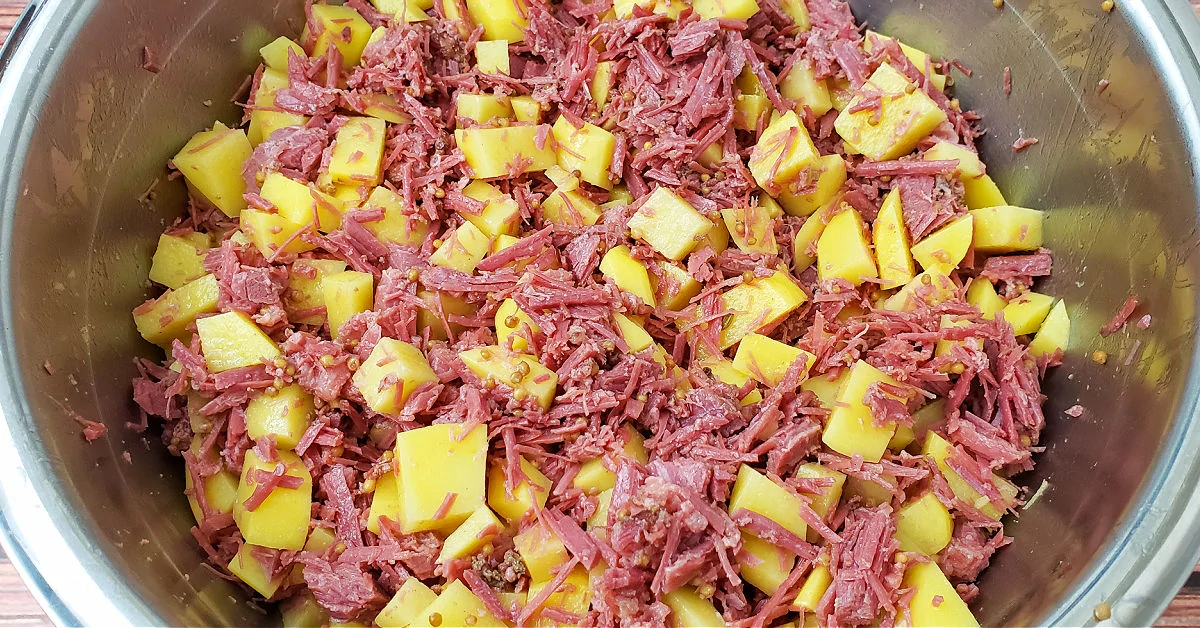 Corned beef and gold potatoes in a metal mixing bowl.
