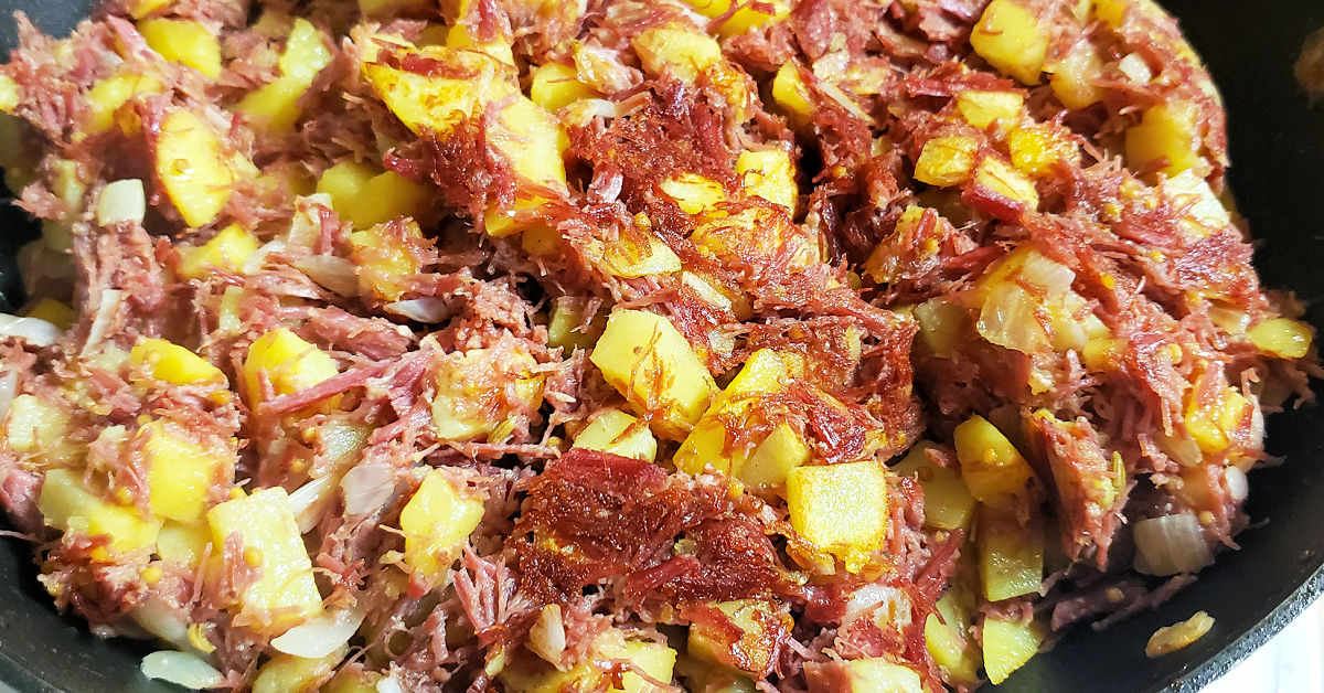 Browned corned beef and potatoes cooking in pan.