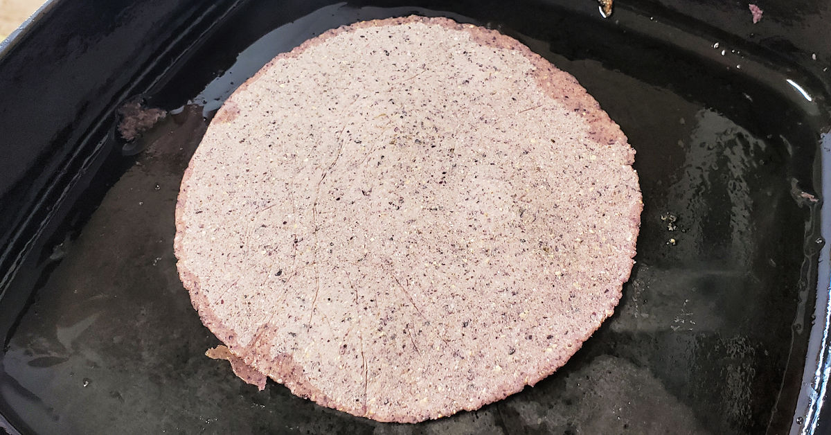 Blue corn tortillas being cooked in a cast iron skillet.