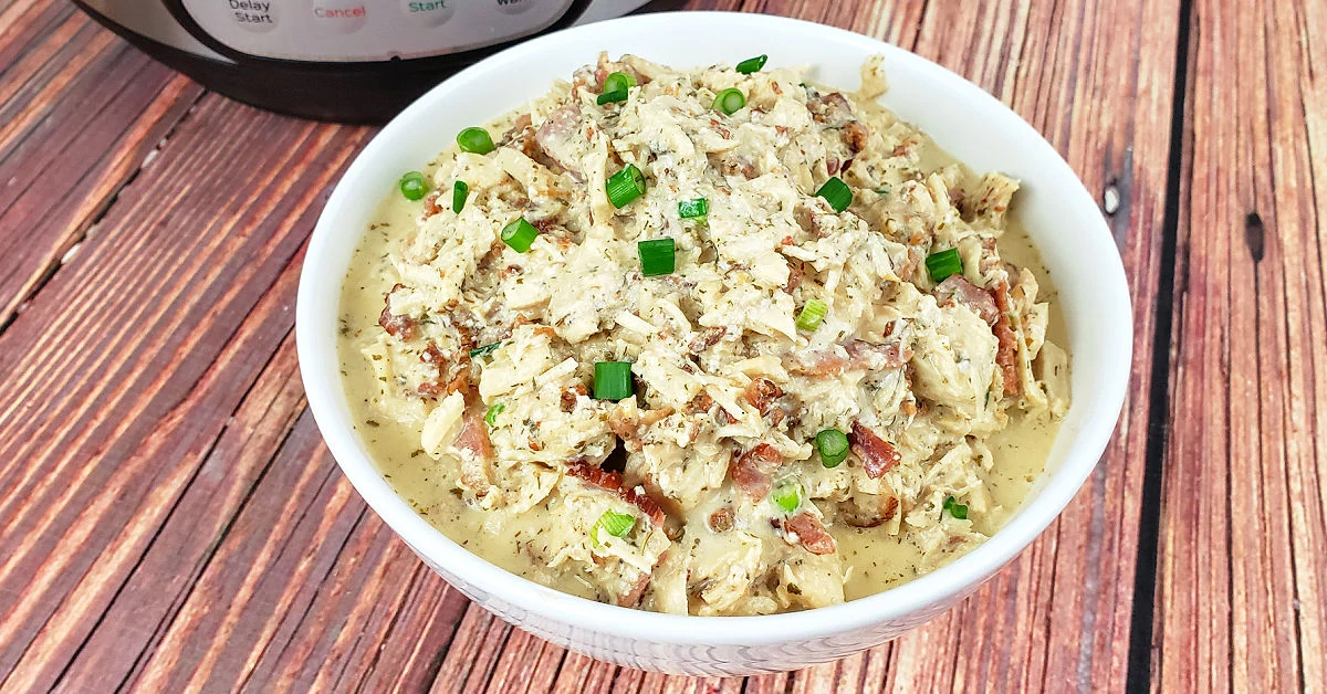 Instant Pot Crack Chicken garnished with fresh green onions in white serving bowl.