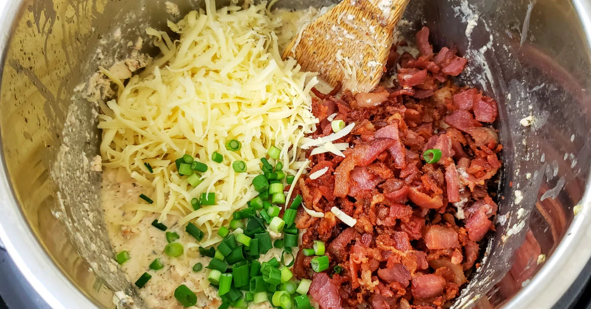 Cheddar cheese, crispy bacon and green onions on top of cheesy chicken mixture in Instant Pot.