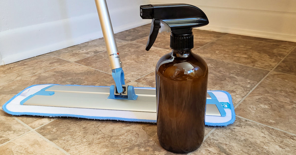 Brown glass spray bottle of floor cleaner and microfiber mop in bathroom.