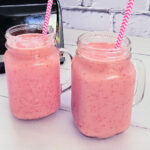 Two pint jars filled with homemade Strawberry Banana Smoothies and served with a pink and white chevron paper straw.