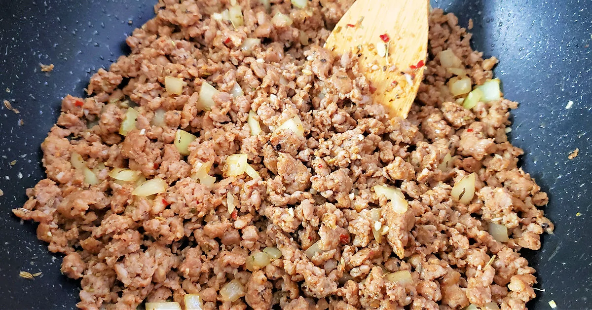 Diced onion and minced garlic being stirred into browned ground sausage.