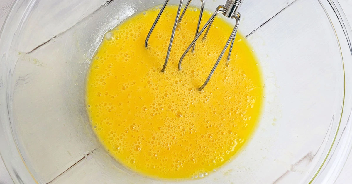 Butter, vanilla extract and eggs being beaten with an electric hand mixer.