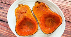 Two roasted honeynut squash halves drizzled with maple syrup on a white serving platter.