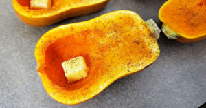 Honeynut squash half with a teaspoon of butter in the open cavity and seasoned with salt, pepper and cinnamon.