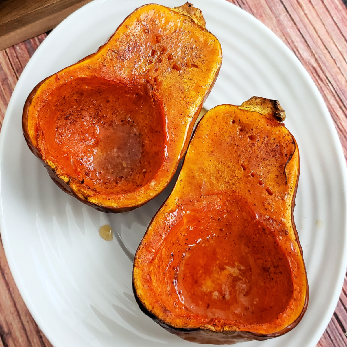 Two roasted honeynut squashes with maple syrup on a white platter.