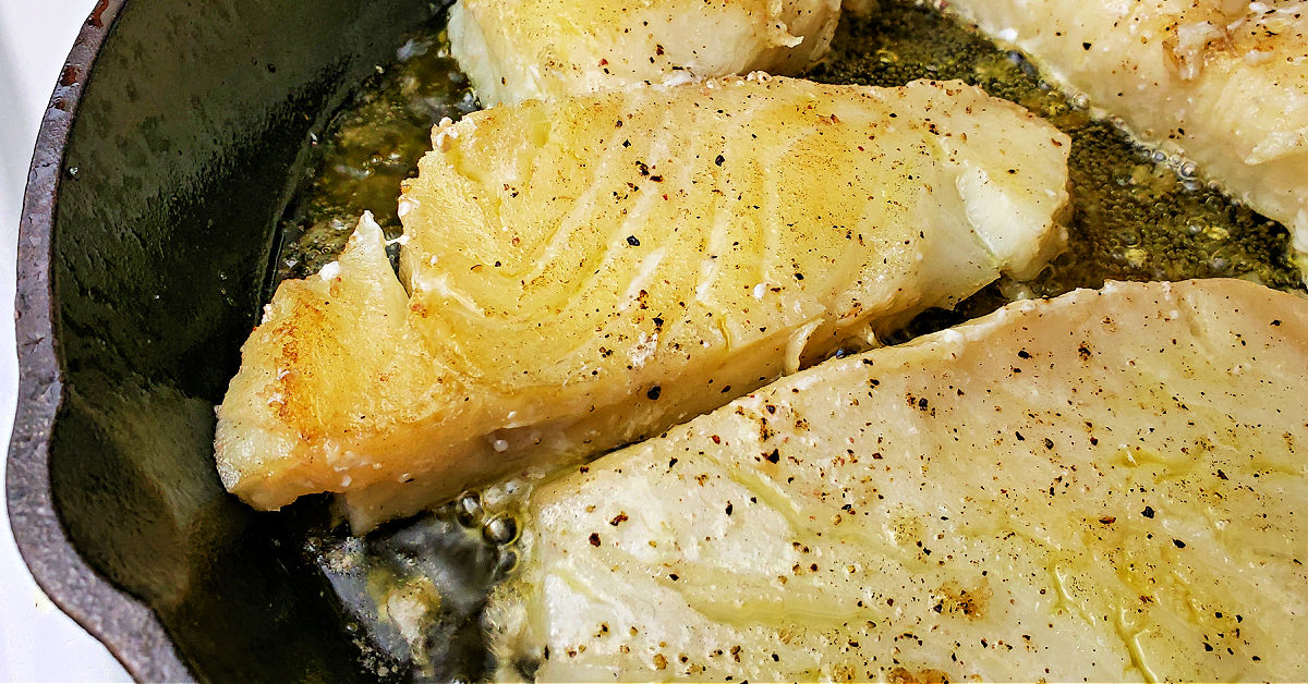 Golden brown Chilean Sea Bass being seared in a cast iron skillet.