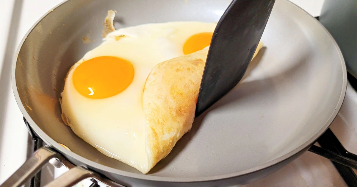 Silicone spatula lifting up eggs frying in Fusion Guard pan with no oil or butter to show how nonstick the pan is.