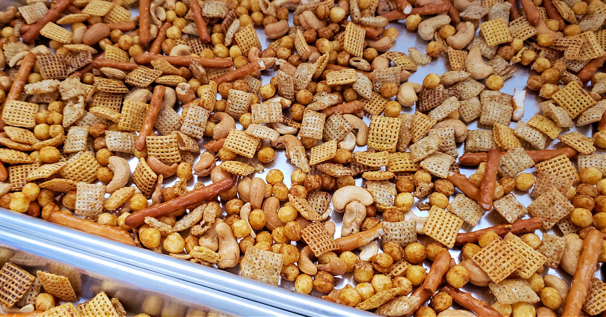 Chex mix being spread out on baking sheets to be baked in the oven.