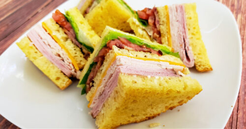 Club sandwich cut into 4 pieces and set on white plate.